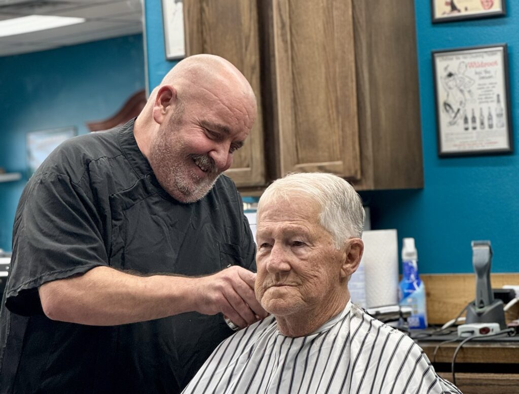 Barber smiling and giving a haircut to an older man at Venice Barbershop, blue wall, classic shop atmosphere