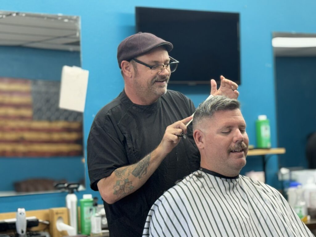 Barber smiling and chatting with a client during a haircut at Venice Barbershop, blue wall, American flag decor, classic shop vibe