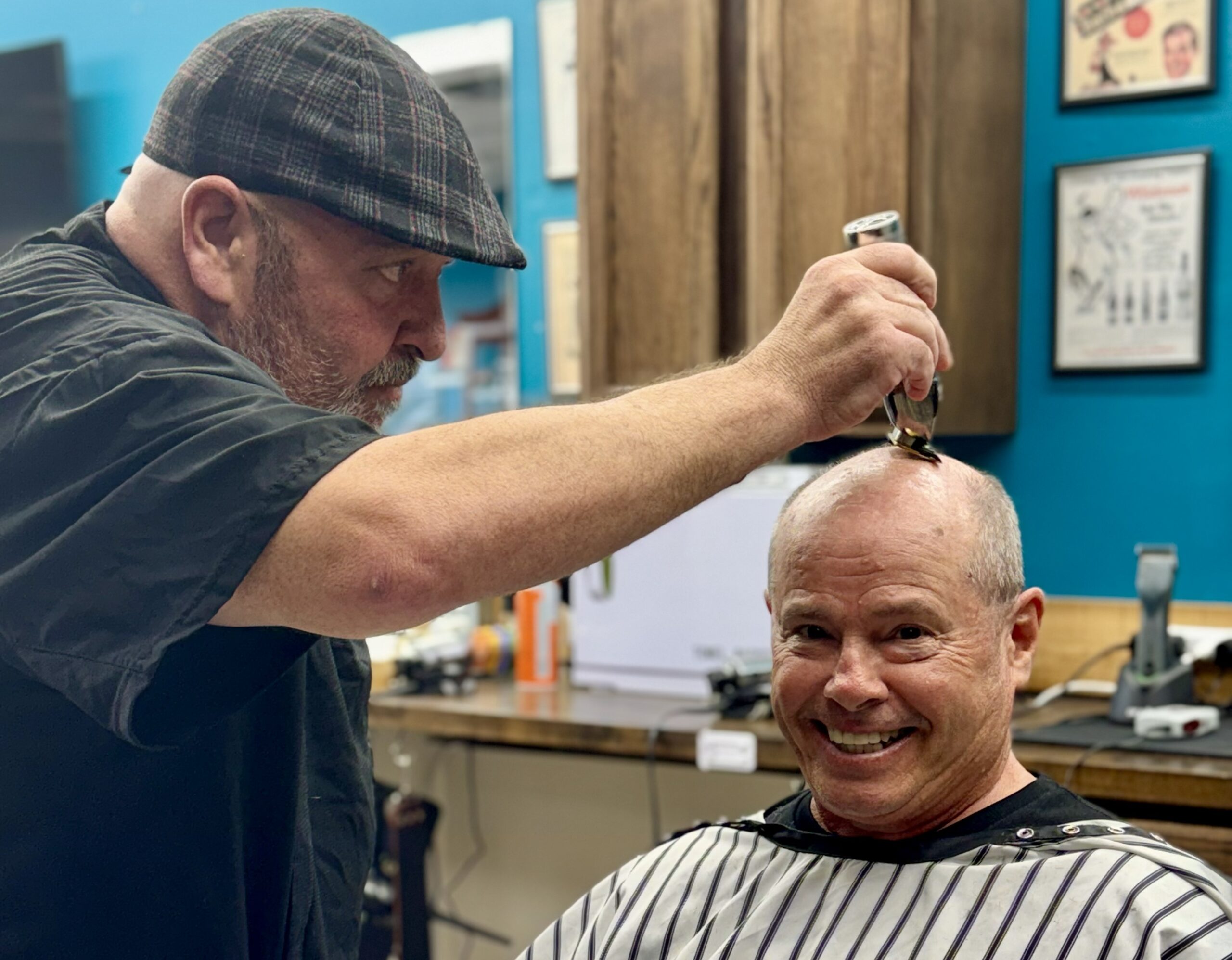 Barber in plaid cap giving a smiling client a close haircut at Venice Barbershop, classic blue wall, vintage decor, community vibe