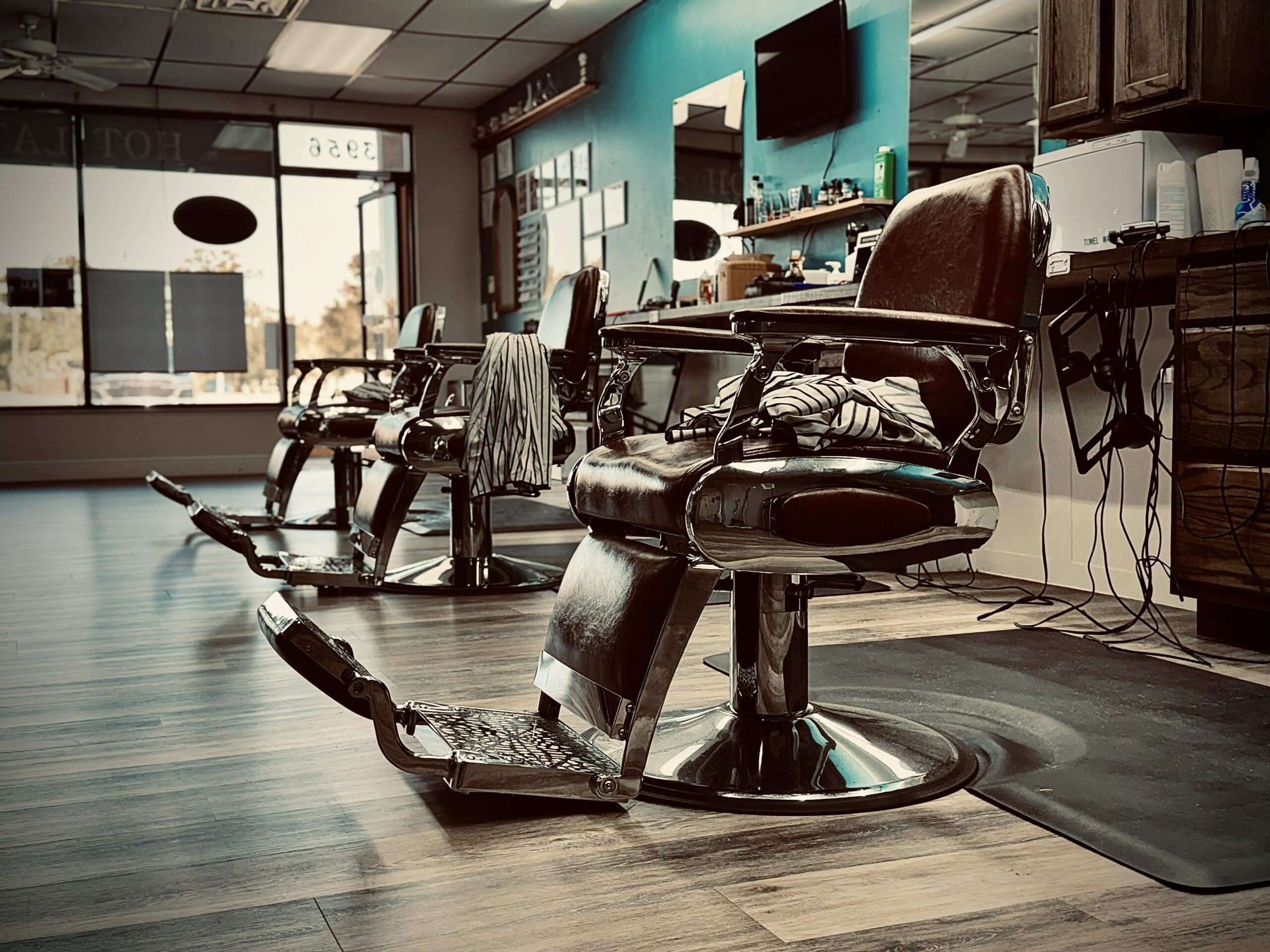 Classic barber chairs in Venice Barbershop, striped capes, blue wall, and sunlit windows, clean and welcoming walk-in barbershop